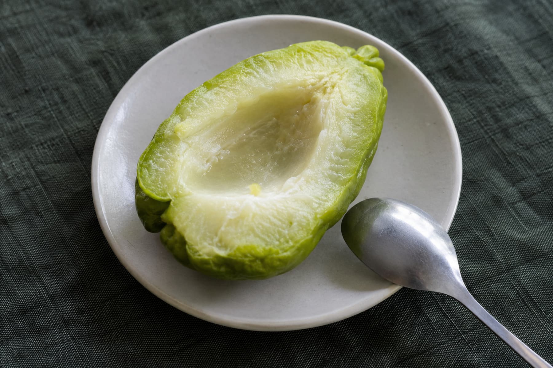 숟가락 옆 접시에 놓인 익힌 차요테 반쪽